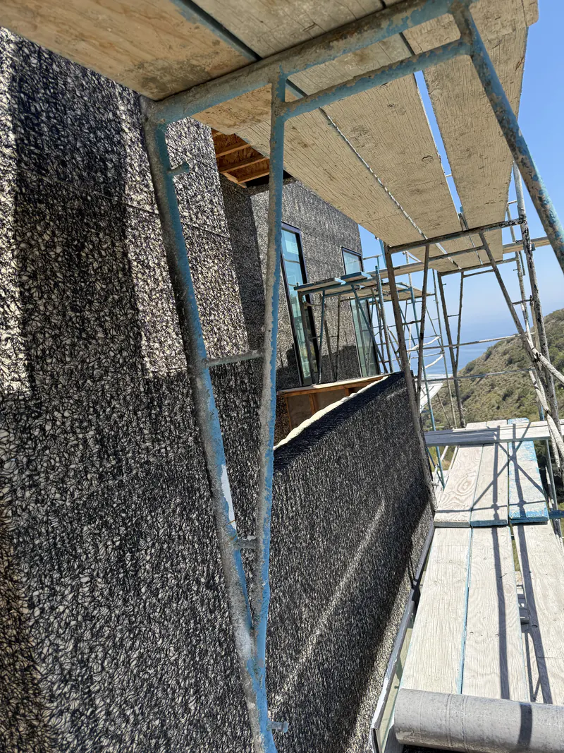 Above grade waterproofing being spray applied to an exterior wall from scaffolding
