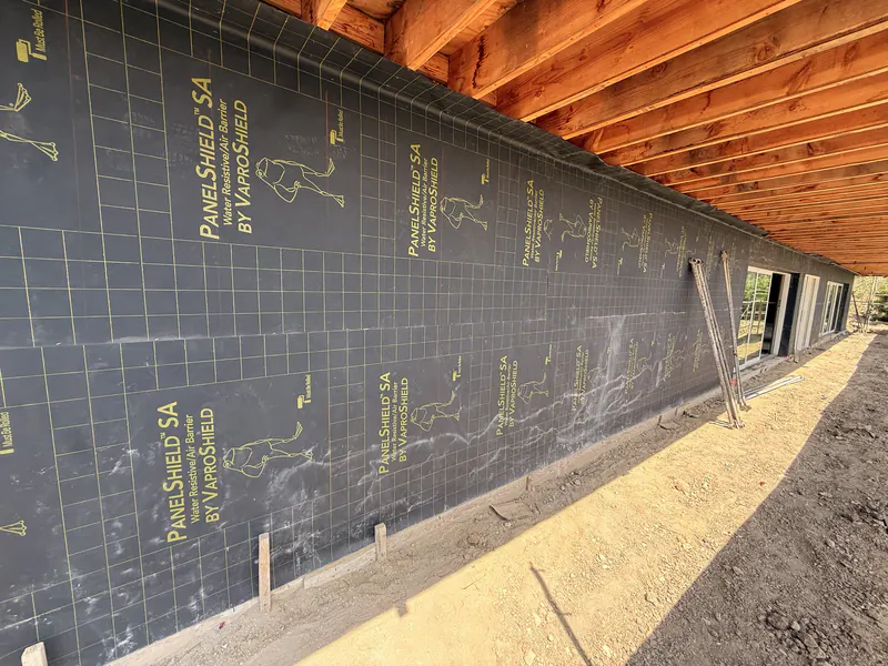 Self adhered air barrier panels installed across an exterior wall under the roof framing