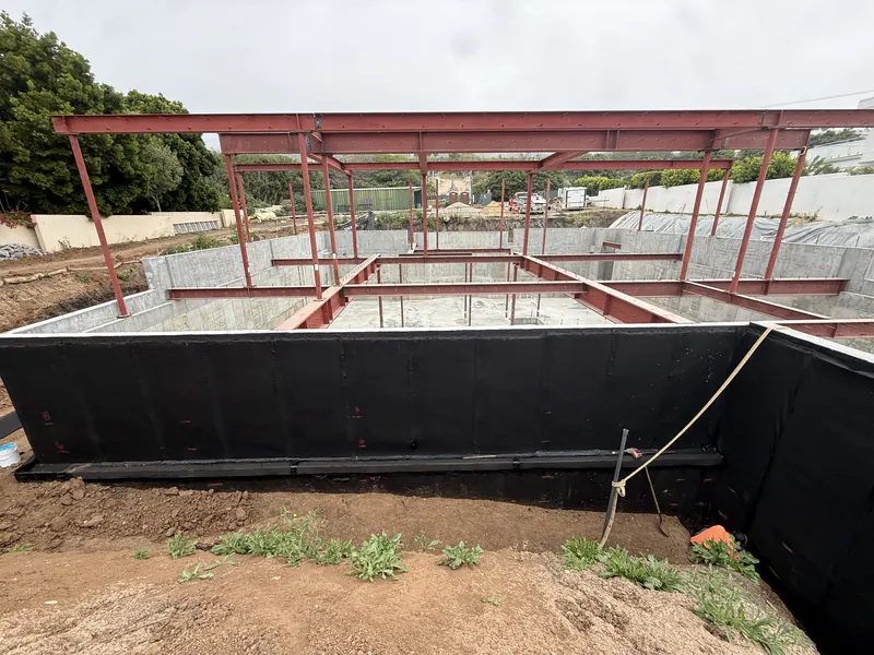 Waterproofing membrane installed on a below grade foundation wall before backfill, with structural steel above