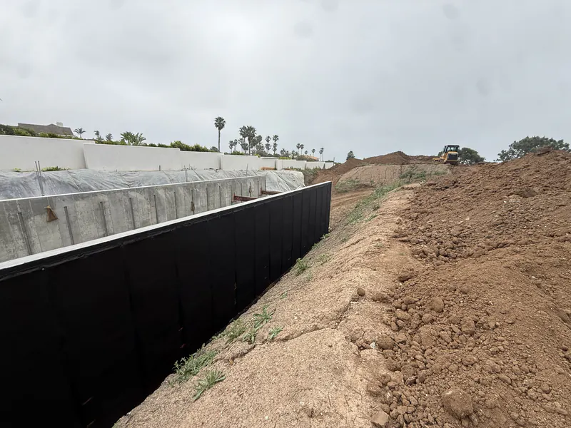 Waterproofed foundation wall inside an open excavation, membrane turned down to the footing