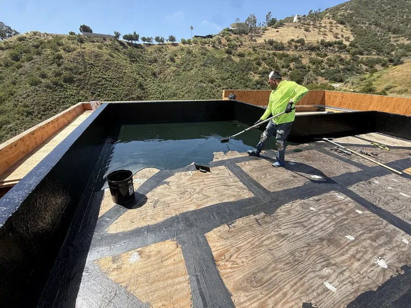 Installer rolling out waterproofing membrane across a below grade deck