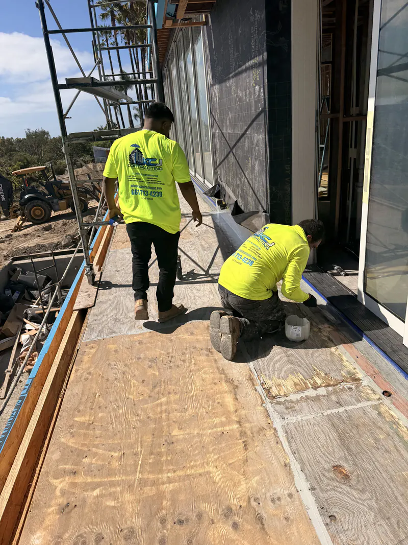 Two KCJ Contracting crew members spray applying a waterproofing coating to an exterior wall