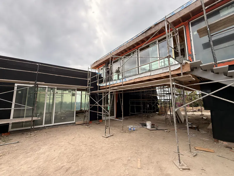Modern glass fronted custom home part way through its weather barrier installation