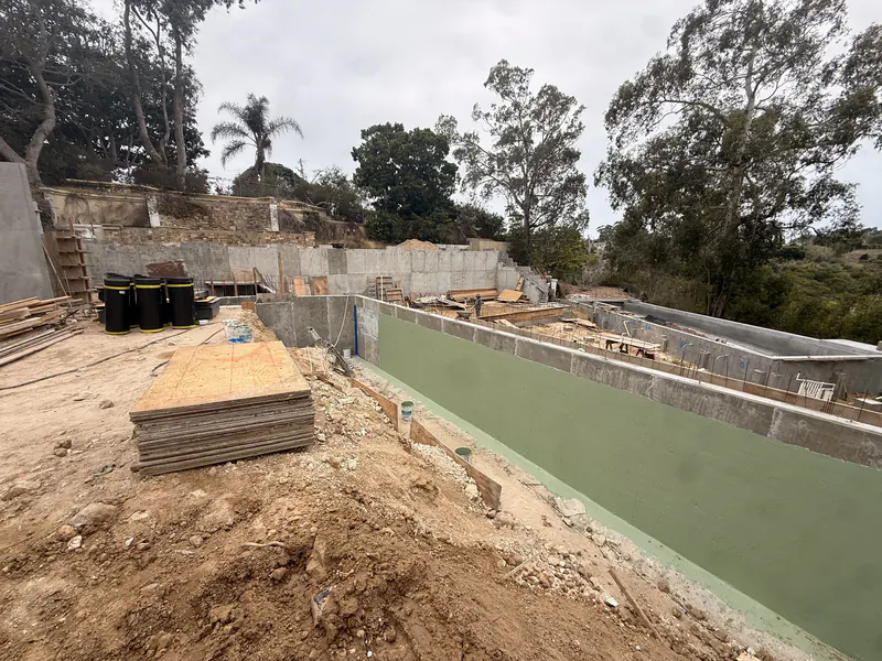 Site retaining wall coated with a waterproofing system before backfill